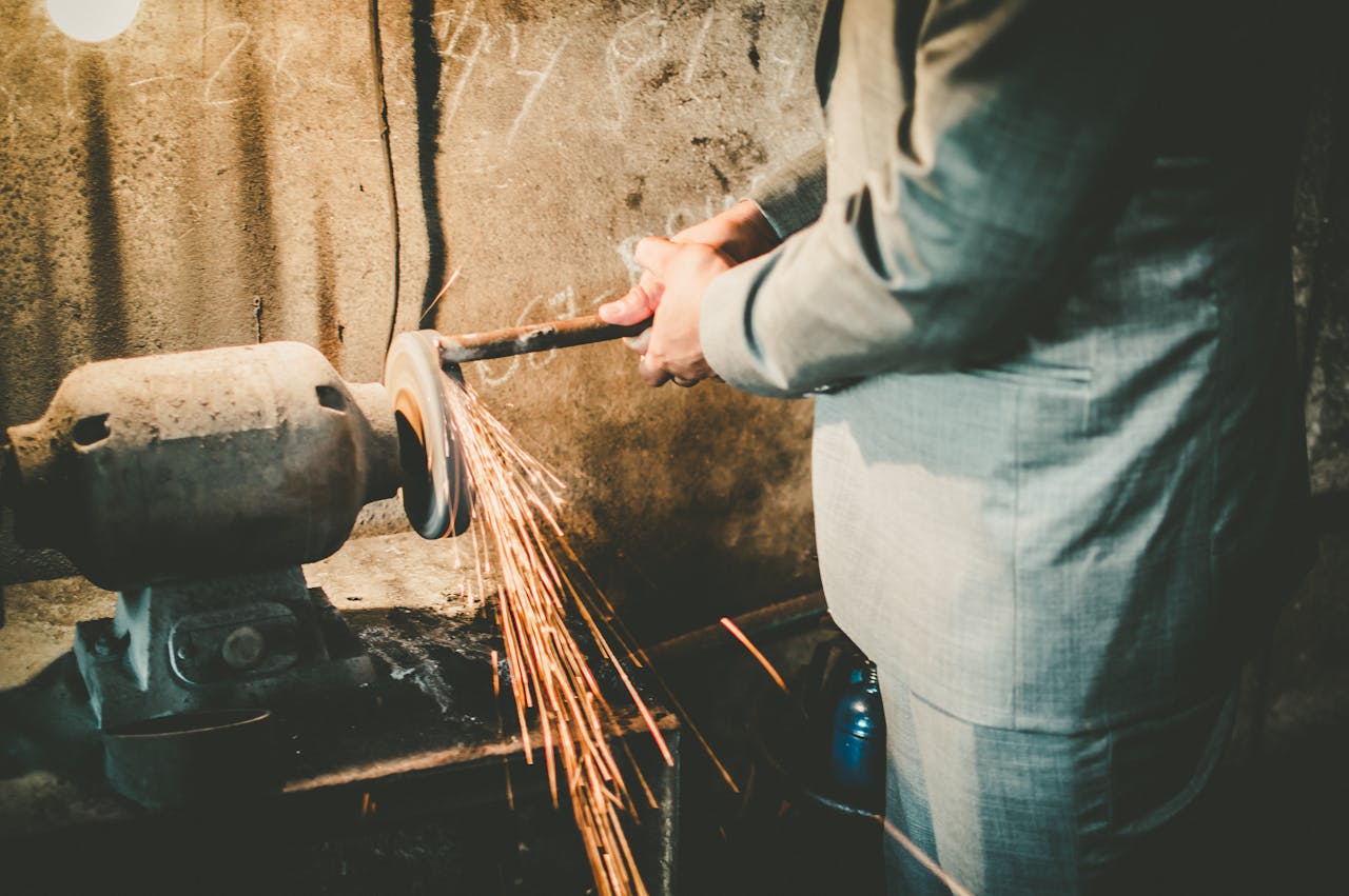 Close-up of a man in a suit using a grinder in an industrial setting with sparks flying.